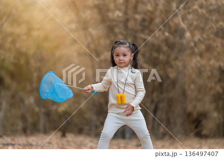 Little child girl holding blue butterfly net exploring the dry forest 136497407