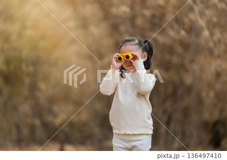 Curious little child girl looking through yellow toy binoculars in dry forest Curious little child girl looking through yellow toy binoculars in dry forest 136497410
