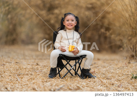 Little child girl sitting on a black folding camping chair in dry field Little child girl sitting on a black folding camping chair in dry field 136497413