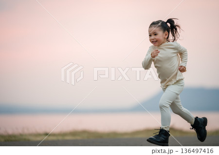 little child girl running happily on an open road by the water at sunset little child girl running happily on an open road by the water at sunset 136497416