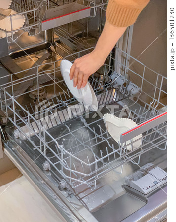 A woman's hand puts dirty dishes in the dishwasher A woman's hand puts dirty dishes in the dishwasher 136501230