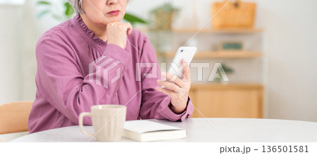 スマホを見ながら不安そうな表情をするシニア女性（詐欺,トラブル,心配） 136501581