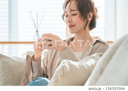 リビングのソファーに座りホットドリンクを飲むオシャレな女性 リビングのソファーに座りホットドリンクを飲むオシャレな女性 136503364