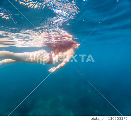 Woman swimming ocean young woman with red hair swims underwater near the surface of clear blue tropical water for a serene vacation experience Woman swimming ocean young woman with red hair swims underwater near the surface of clear blue tropical water for a serene vacation experience 136503375