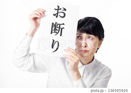 お断りと書かれた紙を持ち迷惑そうな表情の白いシャツを着たシニア女性 136505920