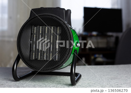 Round heater with radiator for heating room. Protective mesh in front of radiator is included in compact heating design with stand. Ceramic heater with fan in domestic room 136506270