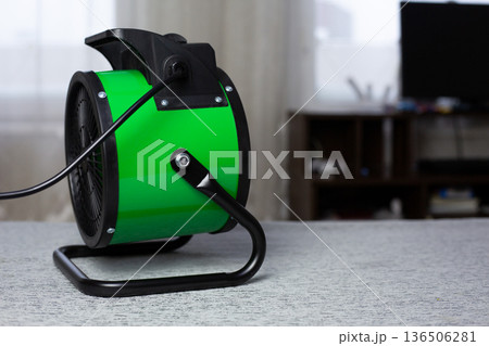 Electric heater with fan blows toward computer desk to warm person workspace at home. The challenges of working from home in cold weather. Raising room temperature with heat gun 136506281