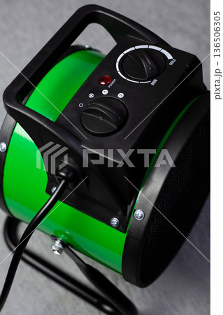 Close-up photo of electric air heater. Green heater with a cord. Plugging the appliance into a power outlet. Insulated cord from powerful home heater, vertical photo Close-up photo of electric air heater. Green heater with a cord. Plugging the appliance into a power outlet. Insulated cord from powerful home heater, vertical photo 136506305