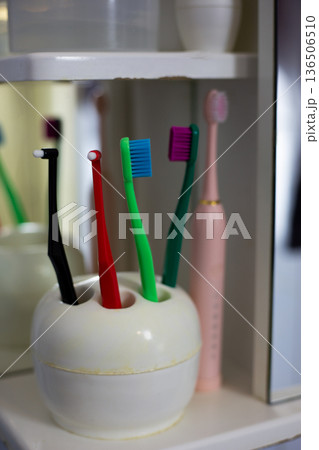 Theme of dentistry through toothbrushes in cup on bathroom shelf. Tools for daily oral care routine. Shelf in lived-in bathroom. Real life with imperfect bathroom interior 136506510