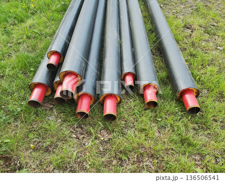 Pre-insulated heating pipes with black outer layer and red inner pipe resting on green grass outdoor storage construction site material 136506541