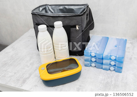 Cooler bag with two bottles of liquid, multiple ice packs, and yellow lunchbox on light surface preparing for transport of cold items Cooler bag with two bottles of liquid, multiple ice packs, and yellow lunchbox on light surface preparing for transport of cold items 136506552
