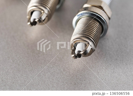 Close up view of two new spark plugs on a gray textured surface, showing metallic threads and ceramic insulator of engine part Close up view of two new spark plugs on a gray textured surface, showing metallic threads and ceramic insulator of engine part 136506556
