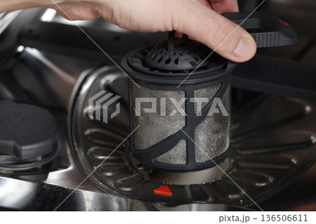 Hand removing dirty filter from dishwasher showing accumulated food residue grime and maintenance process of kitchen appliance 136506611