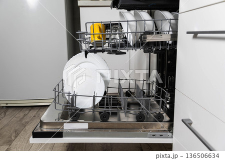 Open modern dishwasher with clean white plates and single yellow ceramic mug positioned on racks, kitchen appliance, household chore completion. Open modern dishwasher with clean white plates and single yellow ceramic mug positioned on racks, kitchen appliance, household chore completion. 136506634