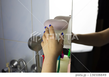 Woman hand reaches for closed soap dish on shelf next to skin care products. Home spa treatment concept. Cleaning products on bathroom shelf. Hand reaches for hygiene product on shelf, POV Woman hand reaches for closed soap dish on shelf next to skin care products. Home spa treatment concept. Cleaning products on bathroom shelf. Hand reaches for hygiene product on shelf, POV 136506649