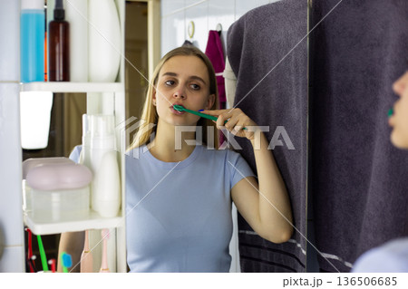 Girl brushing her teeth in front of mirror. Familiar process of daily routine. Oral hygiene with toothbrush. Concept of dental and health care. Reflection of girl in mirror brushing her teeth Girl brushing her teeth in front of mirror. Familiar process of daily routine. Oral hygiene with toothbrush. Concept of dental and health care. Reflection of girl in mirror brushing her teeth 136506685