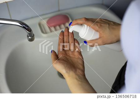 Woman hand squeeze facial cleanser onto her hand. Skin cleanser bottle with special dispenser for saving product. Concept for using skin cleanser foam with convenient packaging Woman hand squeeze facial cleanser onto her hand. Skin cleanser bottle with special dispenser for saving product. Concept for using skin cleanser foam with convenient packaging 136506718