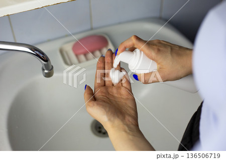 Woman squeezes skincare foam onto her hand from dispenser bottle. Using skincare product. Women hands with facial cleansing and skincare foam, beauty treatment at home in bathroom Woman squeezes skincare foam onto her hand from dispenser bottle. Using skincare product. Women hands with facial cleansing and skincare foam, beauty treatment at home in bathroom 136506719