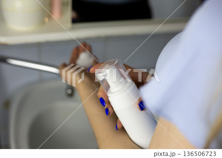 Skin care product in white bottle with dispenser. Bottle of skin cleanser in woman hands in bathroom. Convenient packaging for skin cleansing. Close up of skin care product in hands of young woman Skin care product in white bottle with dispenser. Bottle of skin cleanser in woman hands in bathroom. Convenient packaging for skin cleansing. Close up of skin care product in hands of young woman 136506723
