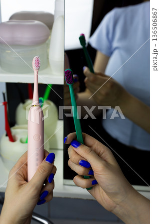 Vertical photo reflecting concept of transition from manual toothbrush to electric toothbrush. Woman holds modern device and conventional one. Modern technologies for cleaning teeth and gums Vertical photo reflecting concept of transition from manual toothbrush to electric toothbrush. Woman holds modern device and conventional one. Modern technologies for cleaning teeth and gums 136506867