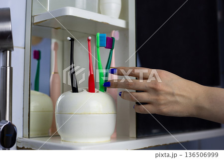 Girl hand reaches for multicolored toothbrush. Bright colors to lift the mood during morning routine. Brushing teeth with brightly colored plastic toothbrush. Taking care of your mouth and breath Girl hand reaches for multicolored toothbrush. Bright colors to lift the mood during morning routine. Brushing teeth with brightly colored plastic toothbrush. Taking care of your mouth and breath 136506999