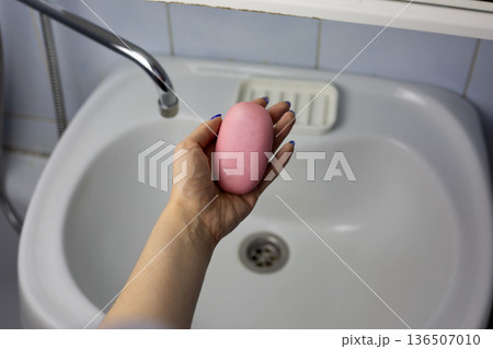 Woman holding soap illustrates concept of handwashing. Natural interior is set against backdrop of hand holding soap. Candid shot demonstrating daily handwashing routine in lived-in bathroom 136507010