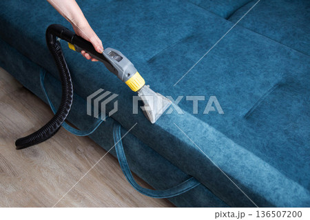 Professional cleaner performing deep cleaning of fabric sofa upholstery with powerful wet vacuum extraction machine, removing dirt and stains, restoring freshness of furniture. Professional cleaner performing deep cleaning of fabric sofa upholstery with powerful wet vacuum extraction machine, removing dirt and stains, restoring freshness of furniture. 136507200