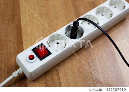 White extension cord with multiple outlets and single red switch and plug from electrical appliance, located on wooden table, demonstrates simplicity and organization in power management White extension cord with multiple outlets and single red switch and plug from electrical appliance, located on wooden table, demonstrates simplicity and organization in power management 136507419