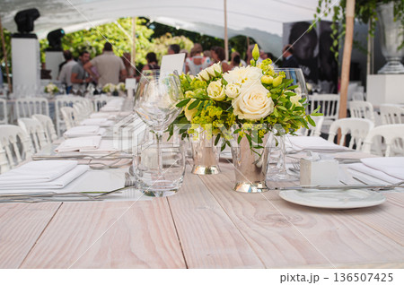 Elegant Outdoor Wedding Table Setting With White Roses, Glassware, And Floral Centerpiece Under Tent 136507425