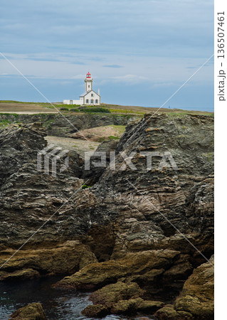 Lighthouse On Rugged Coastline: White Building With Red Roof Beside Jagged Rocks 136507461