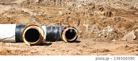 Large black and yellow pipes are placed on the ground at a construction site with dirt and sand around them during the day 136508390