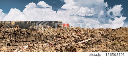 Construction workers are moving dirt at a work site. Clouds build in a blue sky above heavy machinery and fresh earth during the day 136508393