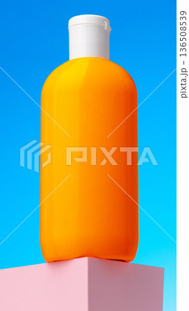 Bright orange bottle stands on a pink platform under a blue sky 136508539