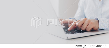 Person types on laptop while sitting at a desk in a bright room during the day 136508566