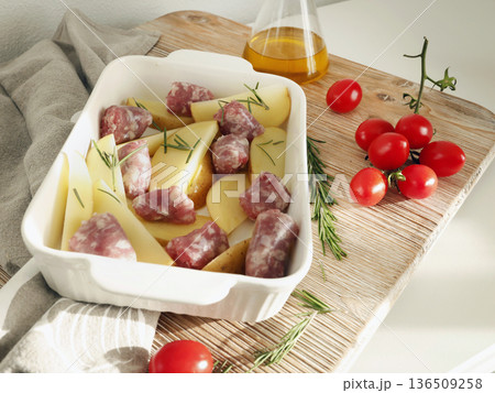 Potato wedges and homemade sausages made from farm-raised meat, prepared for baking in ceramic dish. Food and health. Spices and natural products. 136509258