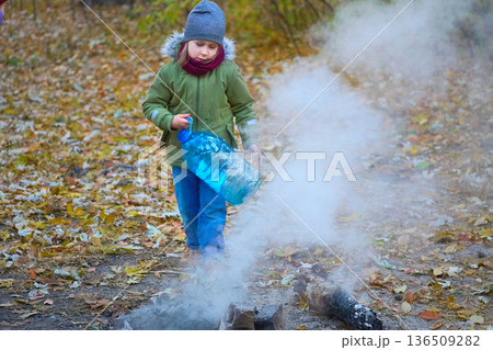 Camp.Child puts out a fire after picnic in autumn forest Camp.Child puts out a fire after picnic in autumn forest 136509282