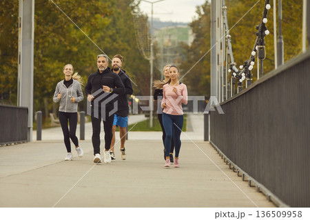 Group of runners jogging together on city bridge in park during fitness training Group of runners jogging together on city bridge in park during fitness training 136509958