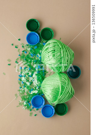 Plastic bottle caps, shredded plastic, and balls of polyester yarn symbolize recycling process and the concept of circular economy and green technologies Plastic bottle caps, shredded plastic, and balls of polyester yarn symbolize recycling process and the concept of circular economy and green technologies 136509991