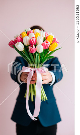 Man in a suit holding a colorful bouquet of tulips tied with a pink ribbon 136511662
