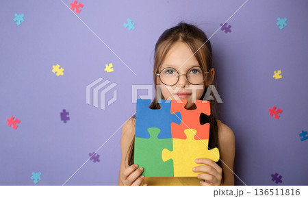 Portrait of schoolgirl holding colorful puzzle pieces symbolizing autism awareness. Inclusive education,  school support, equal learning opportunities and classroom inclusion concept. 136511816
