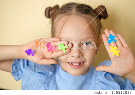 Stickers in the shape of puzzles and hearts decorate the face and palm of a beautiful girl. World Autism Awareness Day. A symbol of education, reason, and people with autism spectrum disorders 136511818