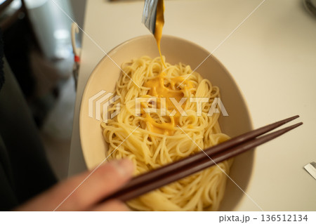 キッチンでパスタソースをかけて麺を食べる男性 136512134