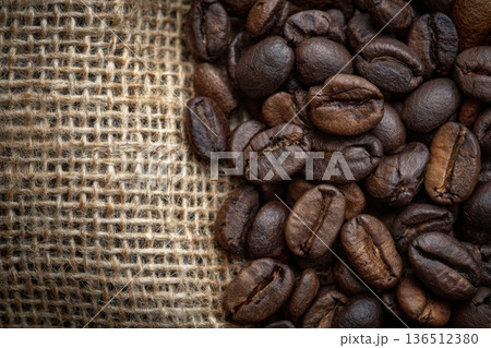Dark coffee beans glisten with rich oils, set against a rustic burlap background, evoking warmth and the art of brewing 136512380