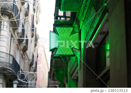 Green LED pharmacy cross illuminating a historic European street building, representing healthcare, medicine, and wellness services at a traditional drugstore Green LED pharmacy cross illuminating a historic European street building, representing healthcare, medicine, and wellness services at a traditional drugstore 136513513