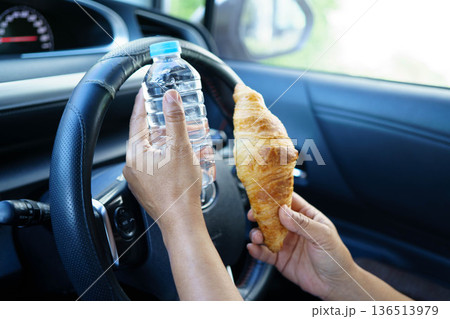 Bangkok, Thailand March 16, 2025 Asian woman driver hold cold water and sandwich bread for eat and drink in car, dangerous and risk an accident. Bangkok, Thailand March 16, 2025 Asian woman driver hold cold water and sandwich bread for eat and drink in car, dangerous and risk an accident. 136513979