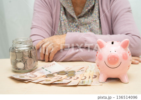 Retired elderly woman counting coins money with piggy bank and worry about monthly expenses and treatment fee payment. 136514096