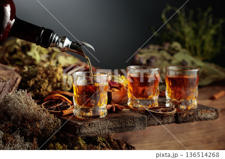 Herbal bitter liqueur is poured from a vintage bottle into a glass. Herbal bitter liqueur is poured from a vintage bottle into a glass. 136514268