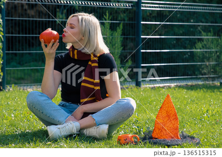 A beautiful girl is sitting on the terrace with a dog, holding a pumpkin in her hand. 136515315