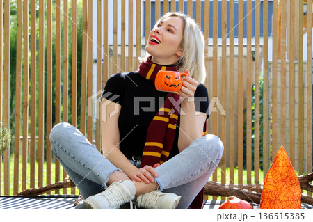 A beautiful girl is sitting on the terrace with a dog, holding a pumpkin in her hand. A beautiful girl is sitting on the terrace with a dog, holding a pumpkin in her hand. 136515385