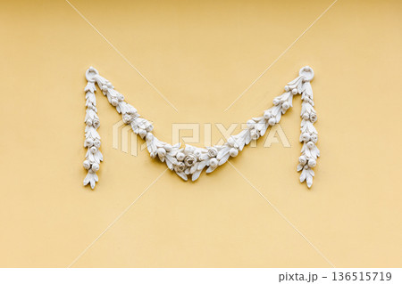 Elegant white plaster garland mounted on yellow wall 136515719